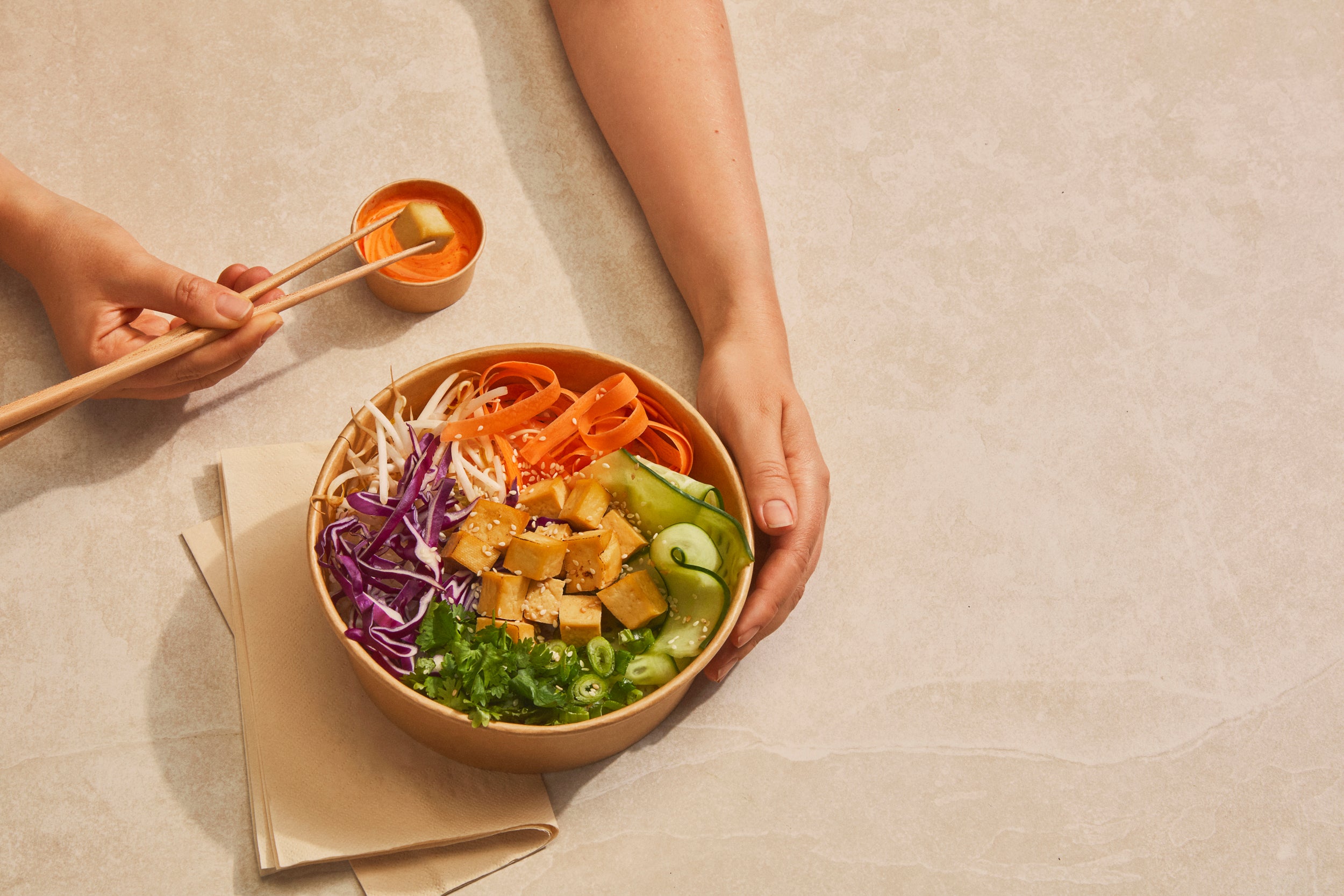 A poke bowl in eco-friendly packaging sits on a table, with a hand holding chopsticks, highlighting sustainable dining solutions.