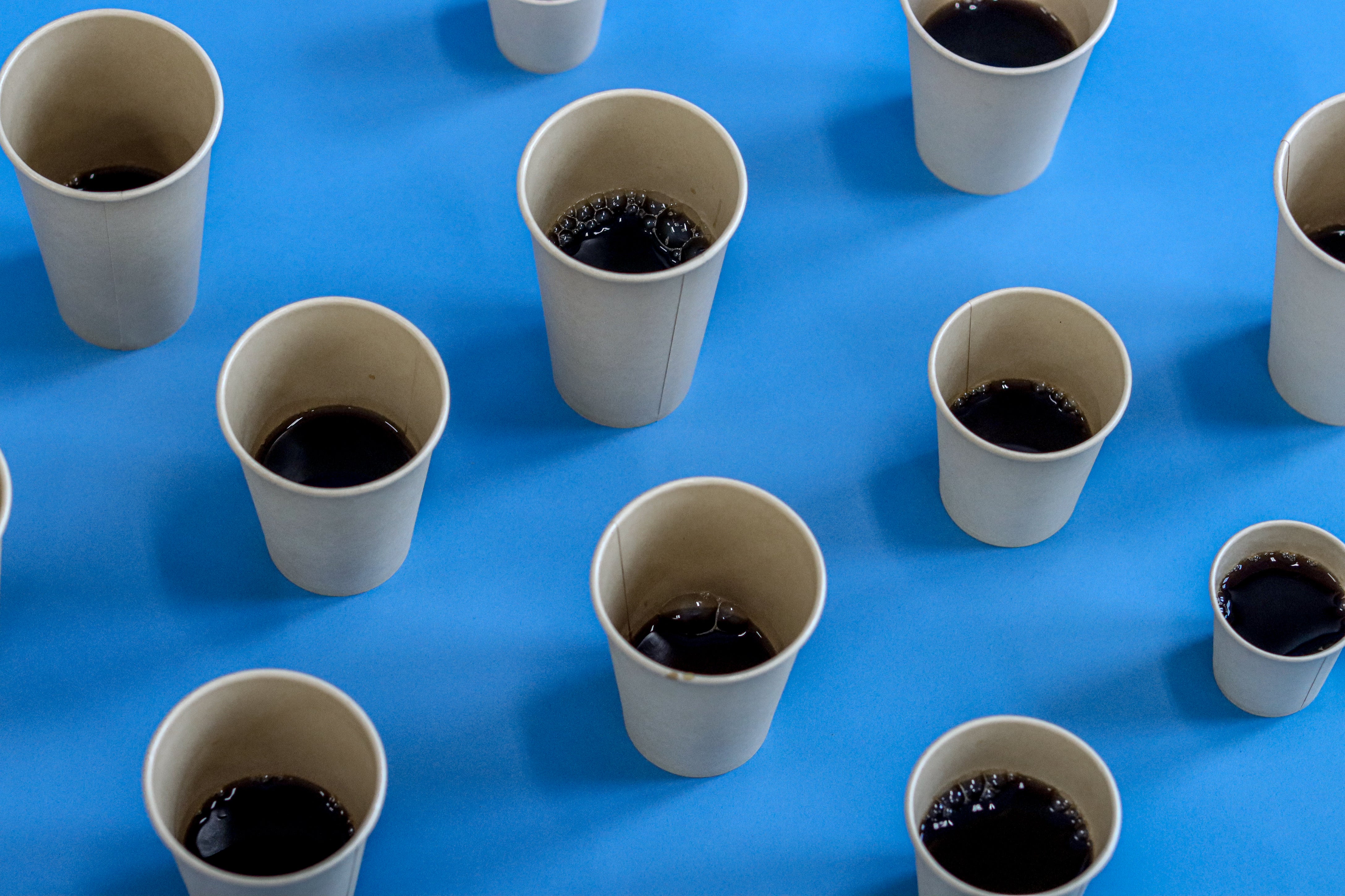 The image shows several bamboo takeaway cups filled with dark coffee, arranged on a blue background.