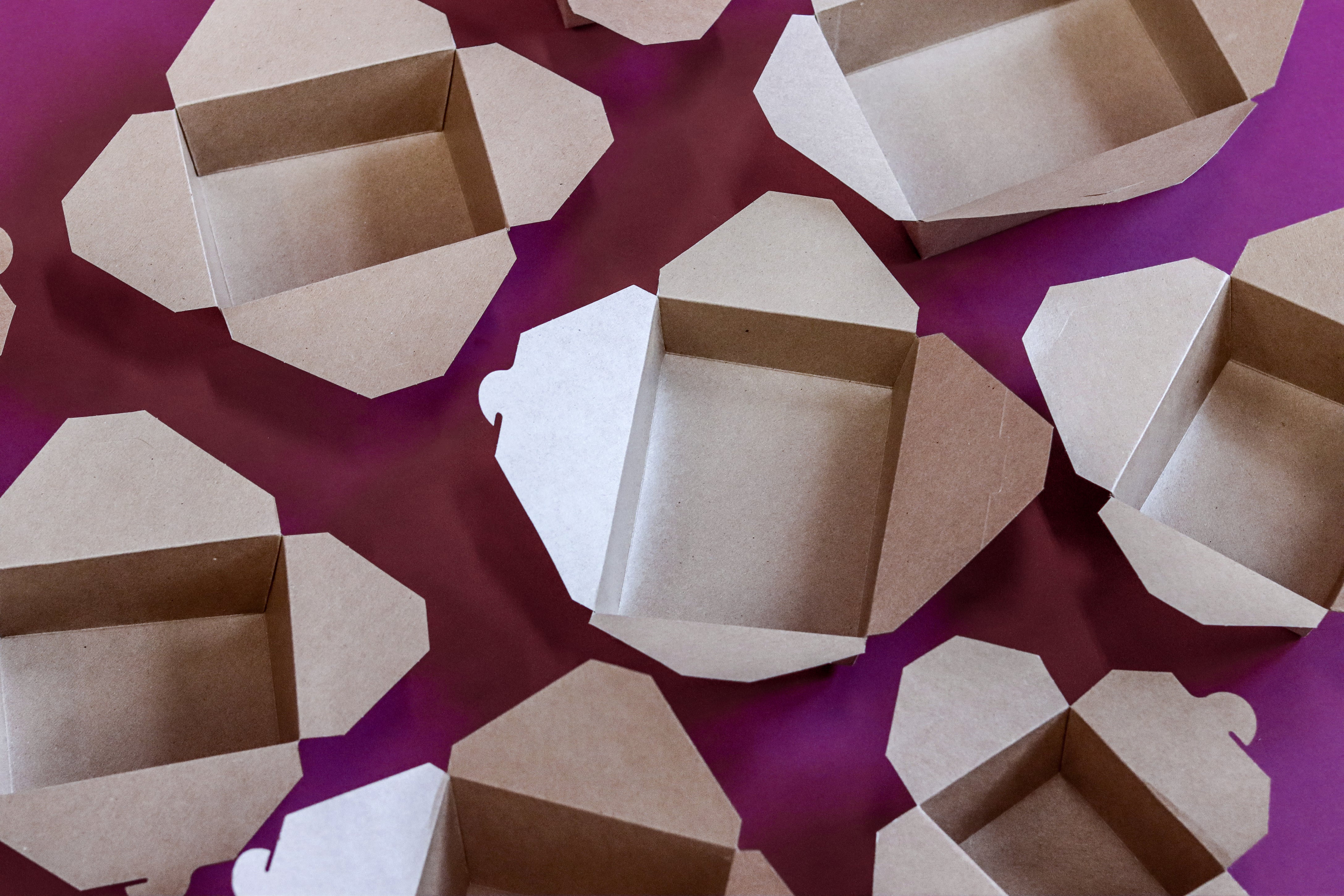 The image features several open, empty Kraft takeaway boxes on a purple background, highlighting a theme of sustainable packaging.