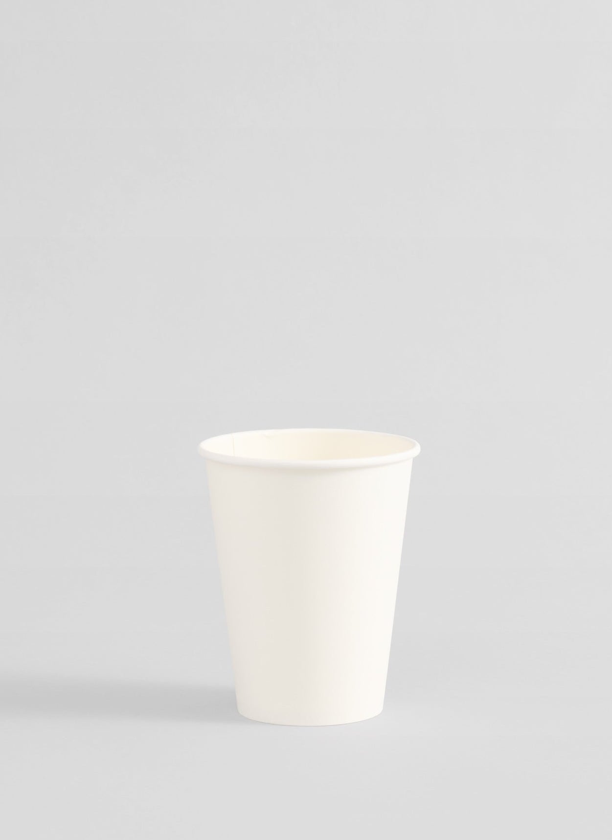 A single white paper cup centered on a light gray studio background.