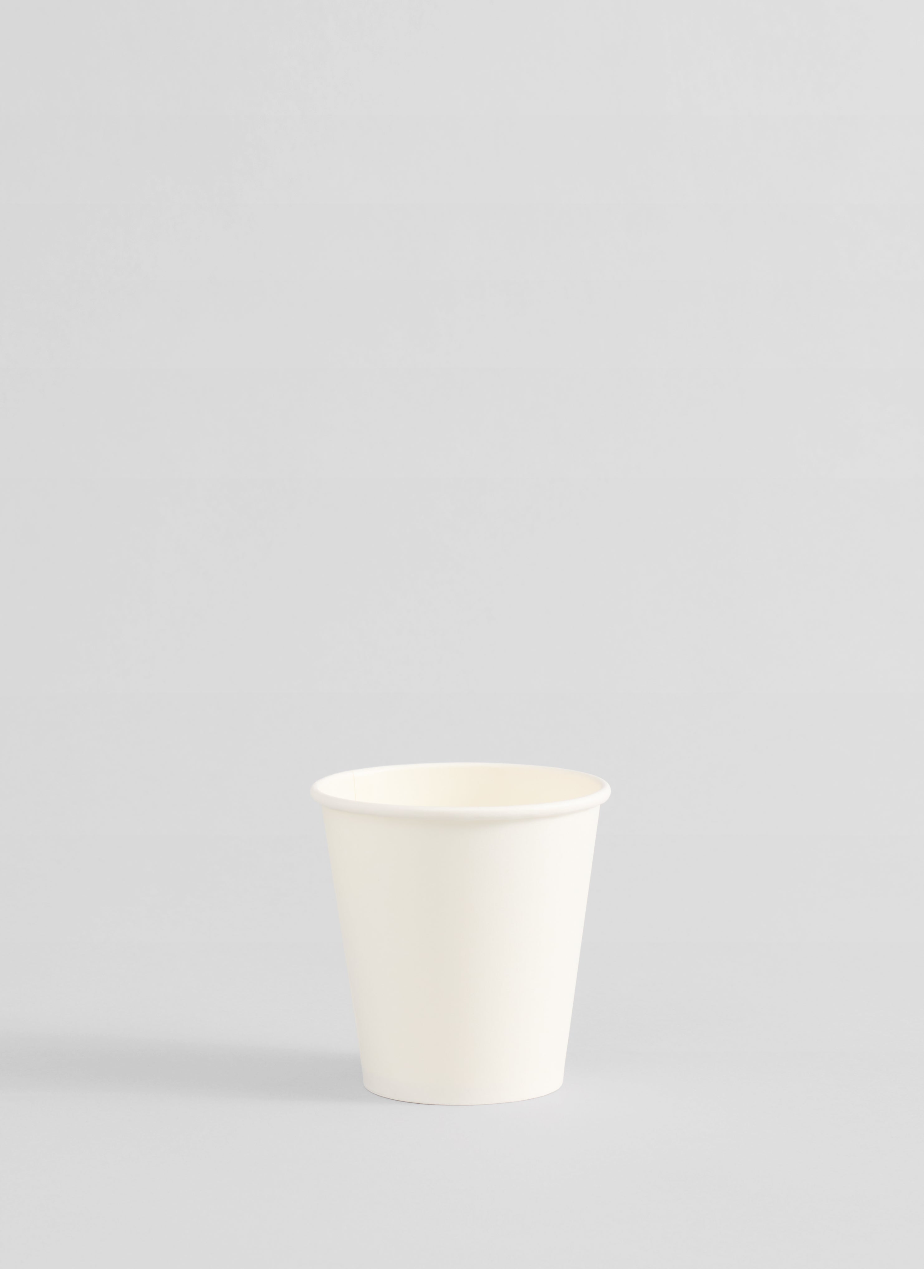 A single small white paper cup centered against a light gray studio background.
