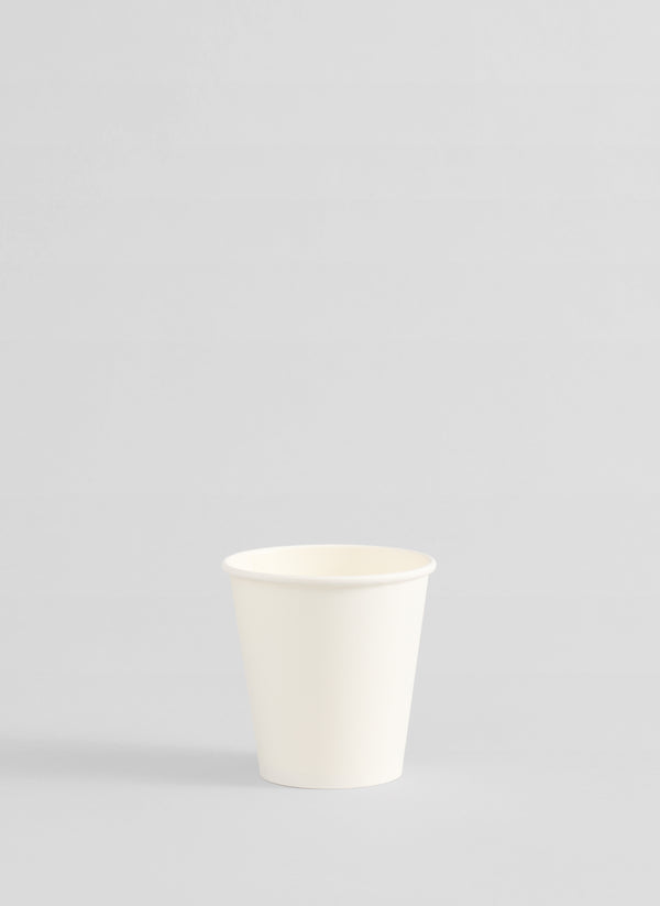 A single small white paper cup centered against a light gray studio background.