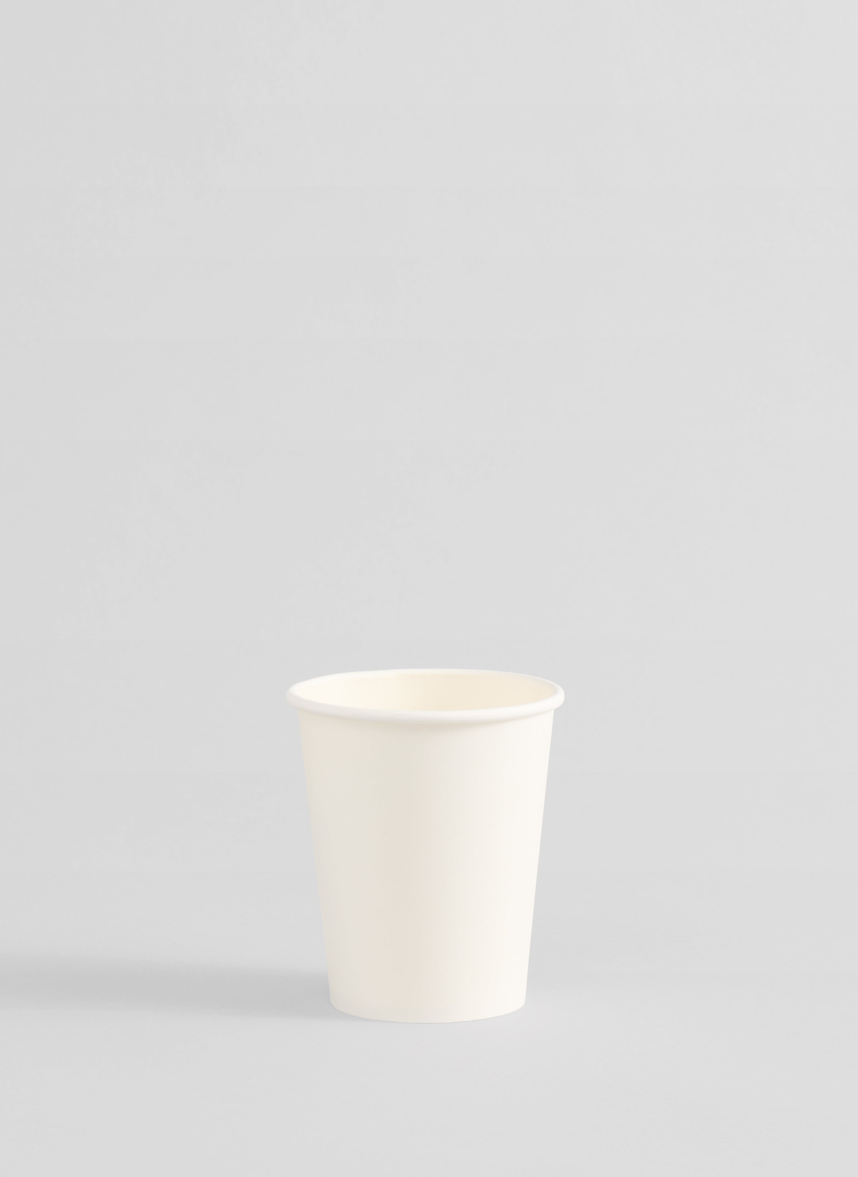 A single small white paper cup centered on a light gray studio background.