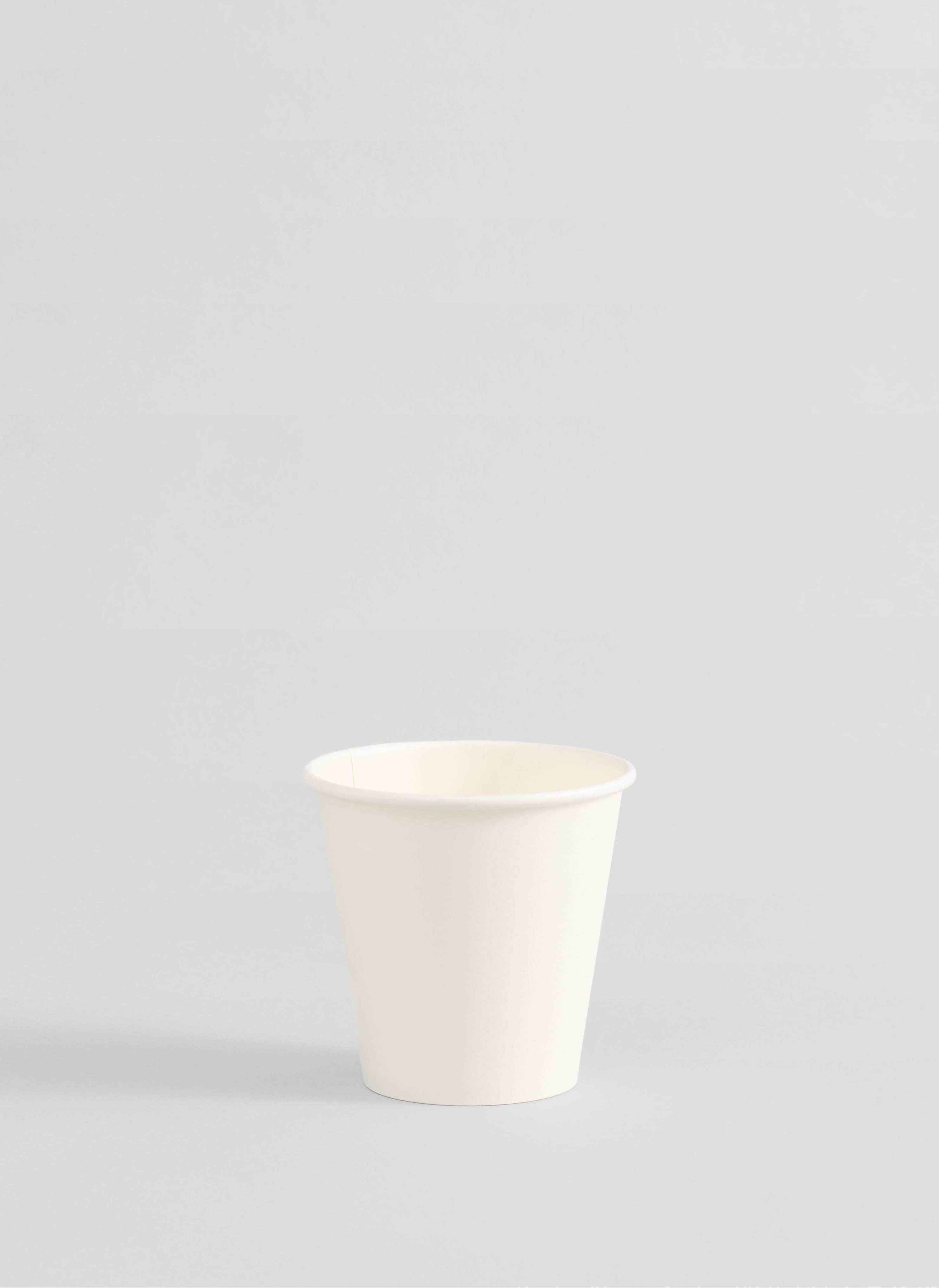 A single white paper cup centered against a solid light gray background.